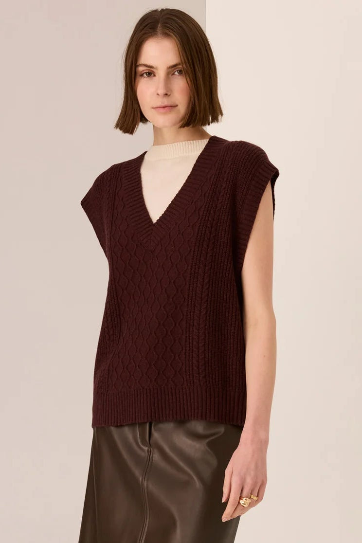 Woman wearing a brown sleeveless sweater and leather skirt on a beige background