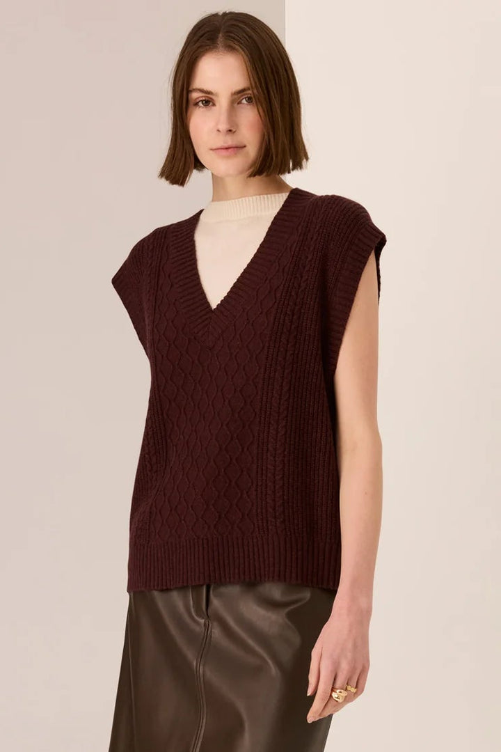 Woman wearing a brown sleeveless sweater and leather skirt on a beige background