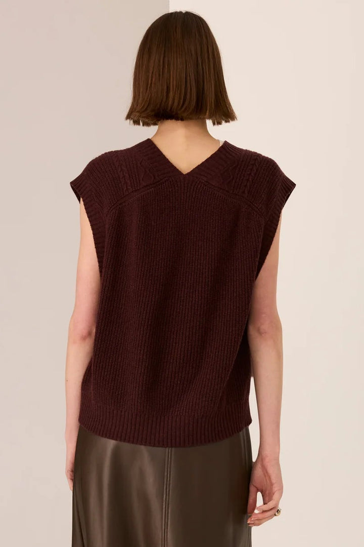 Person wearing a brown sleeveless top and leather skirt on a beige background