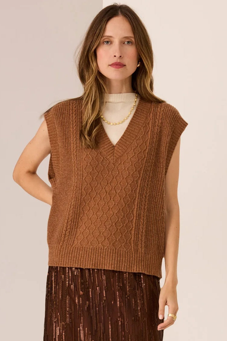 Woman wearing a brown sleeveless sweater and pleated skirt on a beige background
