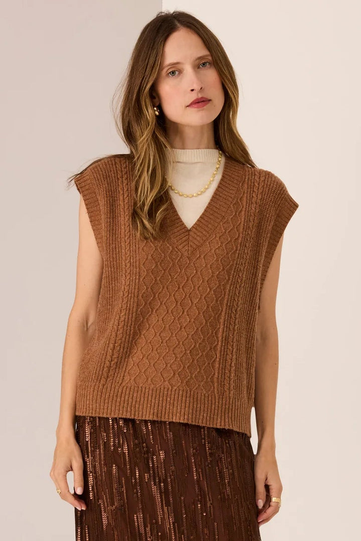 Woman wearing a brown sleeveless top and pleated skirt on a white background