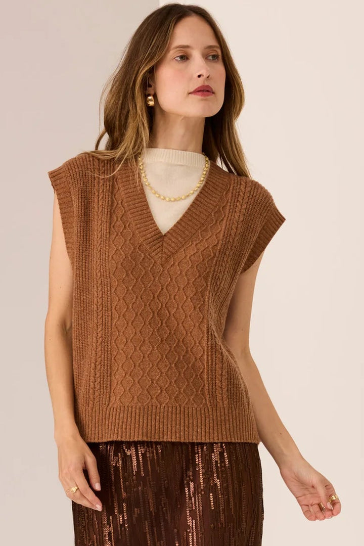 Woman wearing a brown sleeveless top and pleated skirt on a beige background