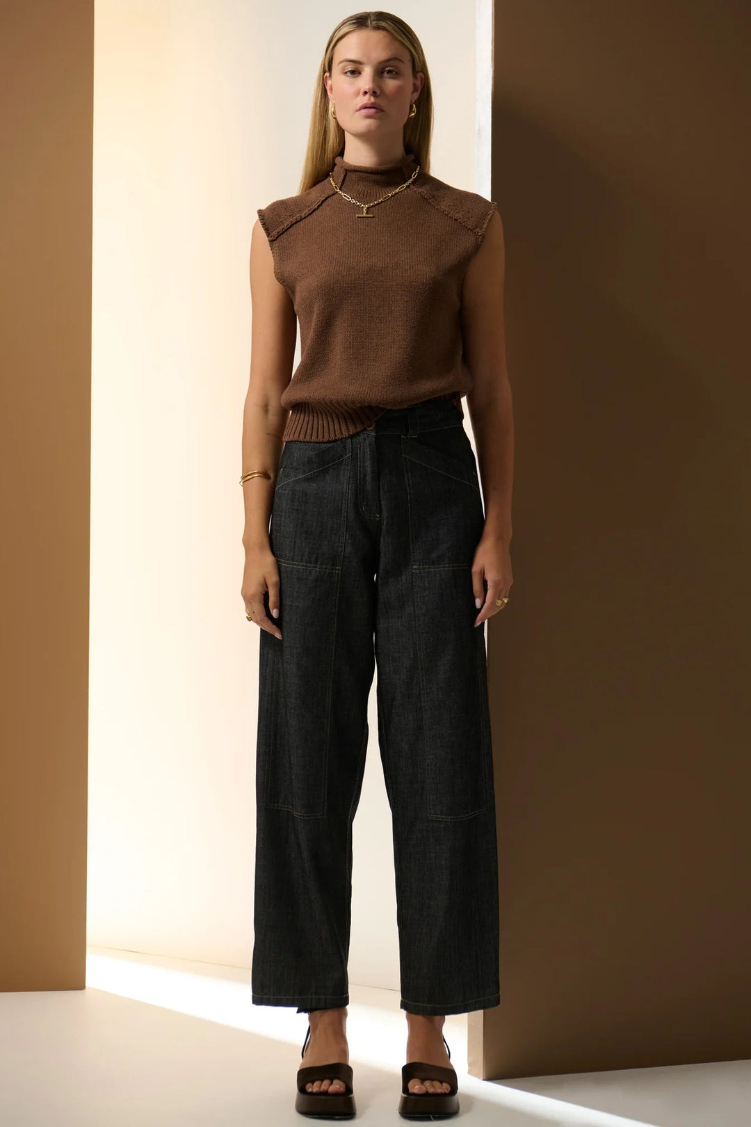Woman wearing a brown sleeveless top and black pants against a neutral background. Pol Muhle Barrel Denim Pant Indigo