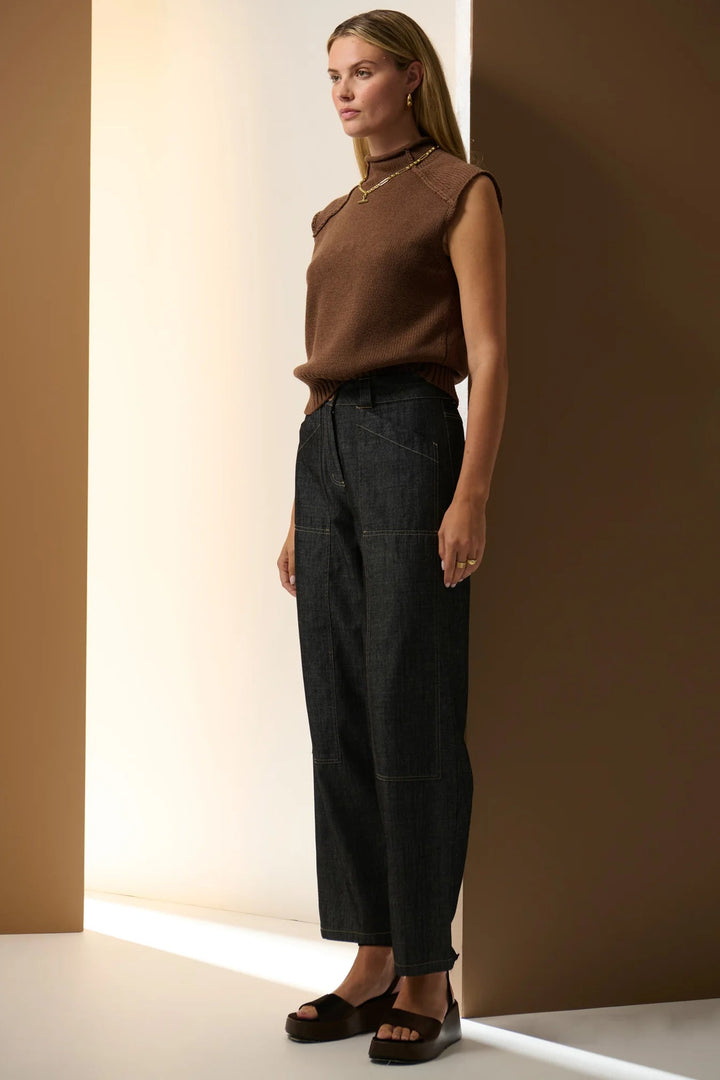 Woman wearing a brown top and black pants against a neutral wall. Pol Muhle Barrel Denim Pant Indigo