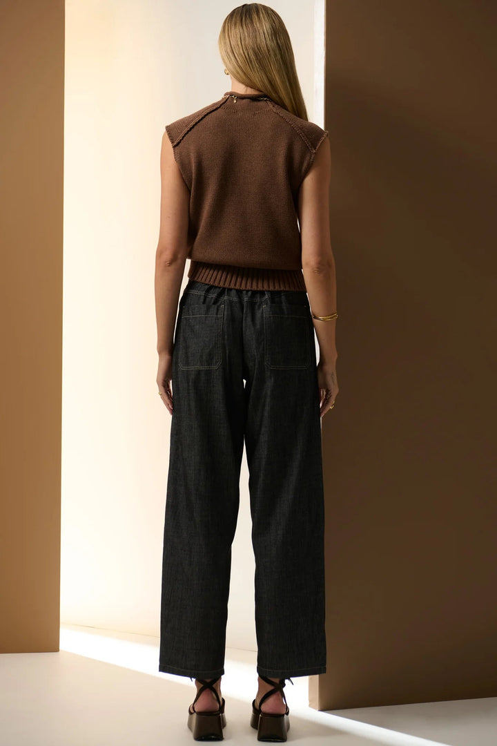 Woman wearing a brown sleeveless top and black pants against a brown wall. Pol Muhle Barrel Denim Pant Indigo