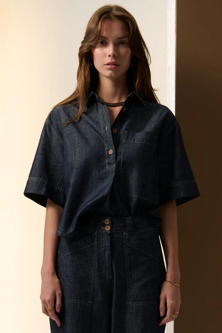 Woman wearing a dark outfit against a neutral background. Pol Muhle Denim Top Indigo