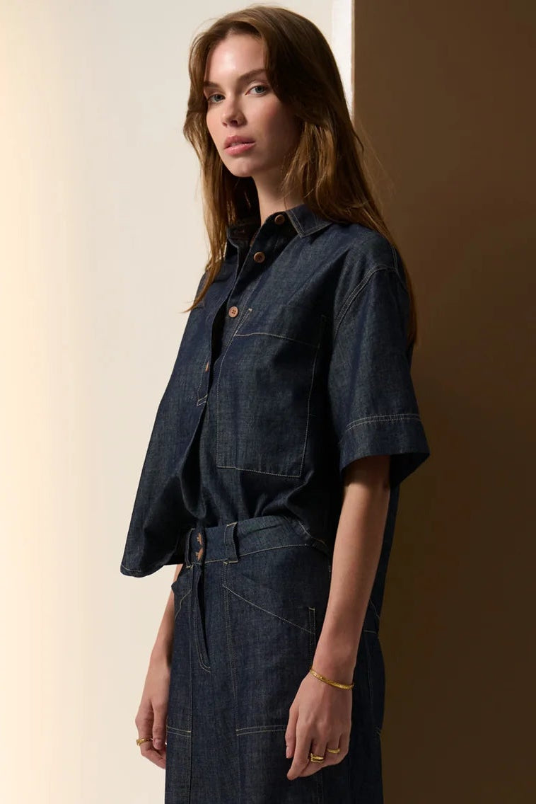 Woman wearing a dark denim jumpsuit against a neutral background. Pol Muhle Denim Top Indigo