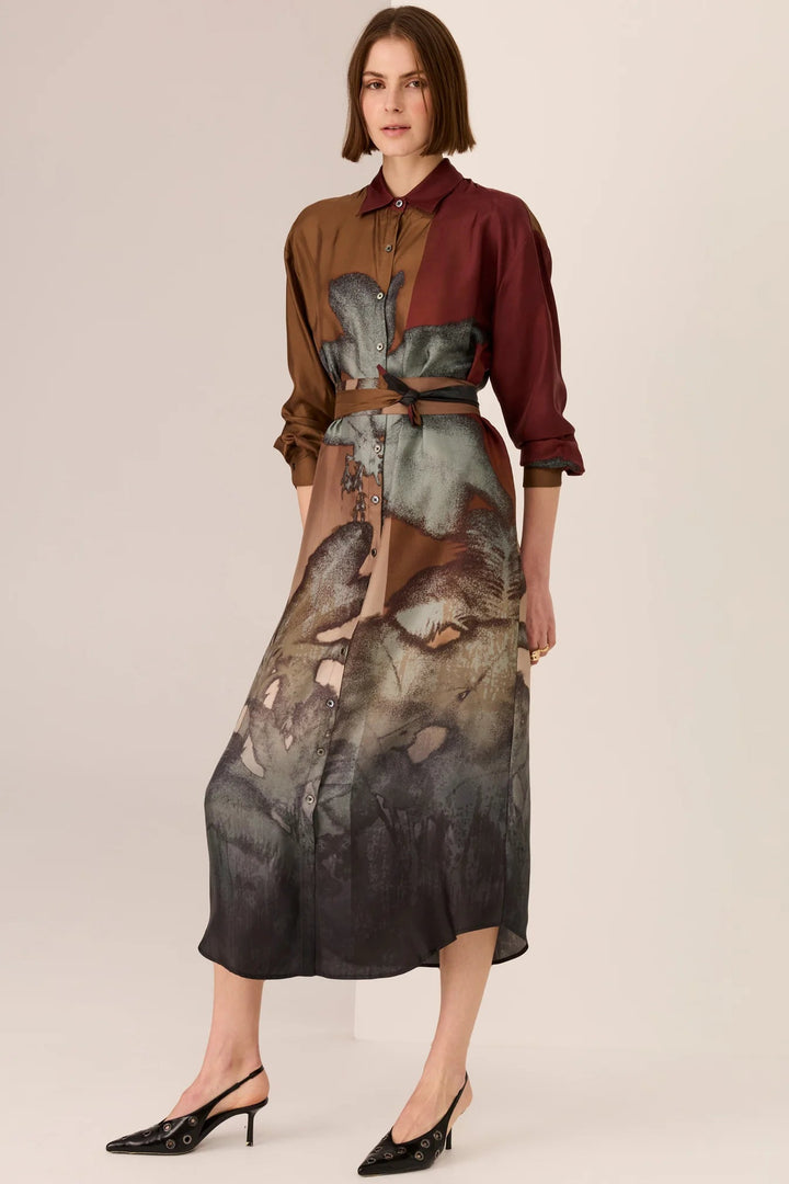 Woman wearing a two-tone shirt and a long, patterned skirt on a plain background
