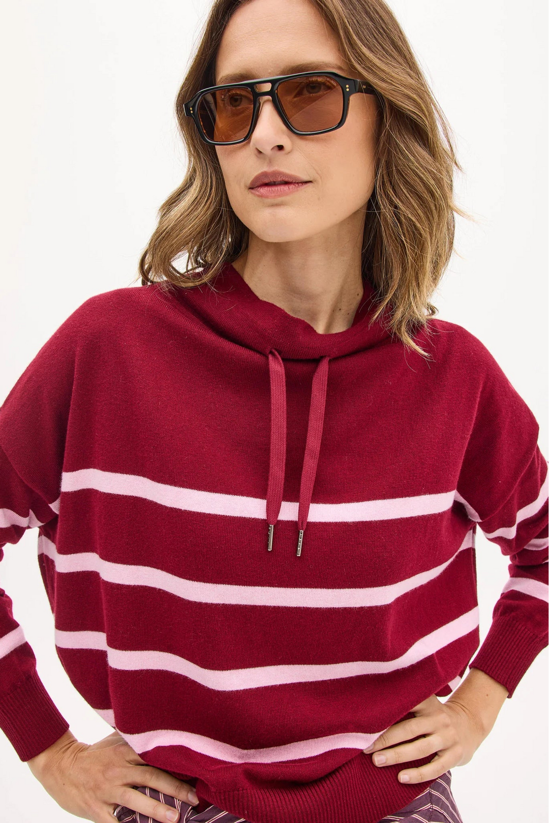 Woman wearing a red and white striped sweater with sunglasses on a plain background