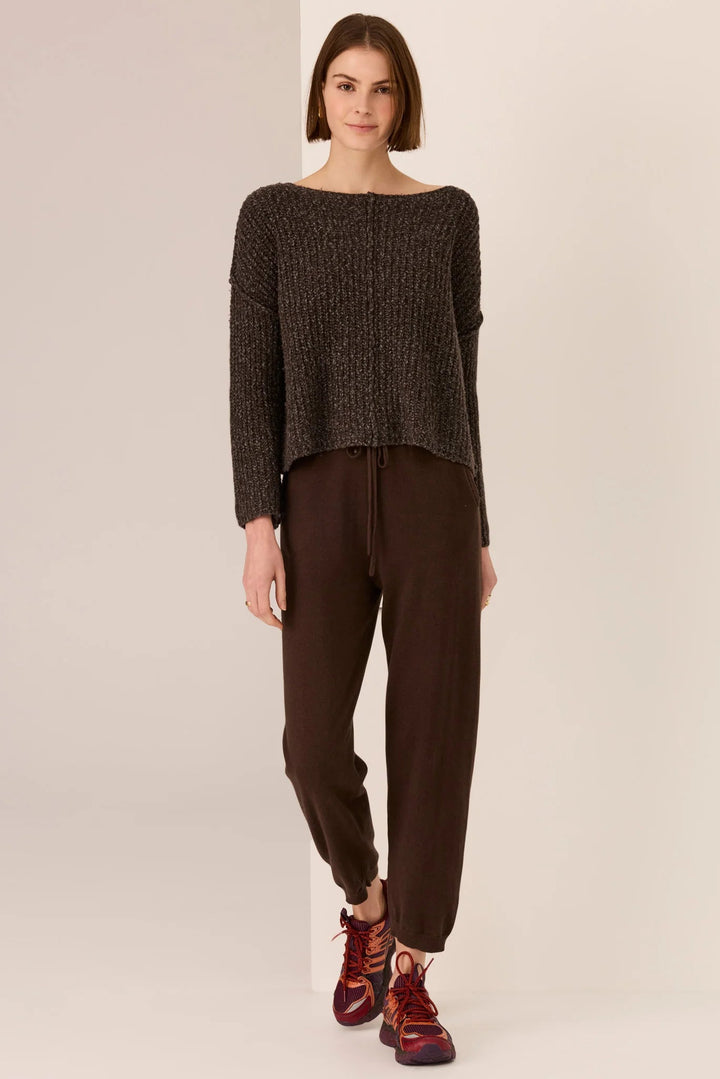 Woman wearing a dark brown sweater and pants on a plain background