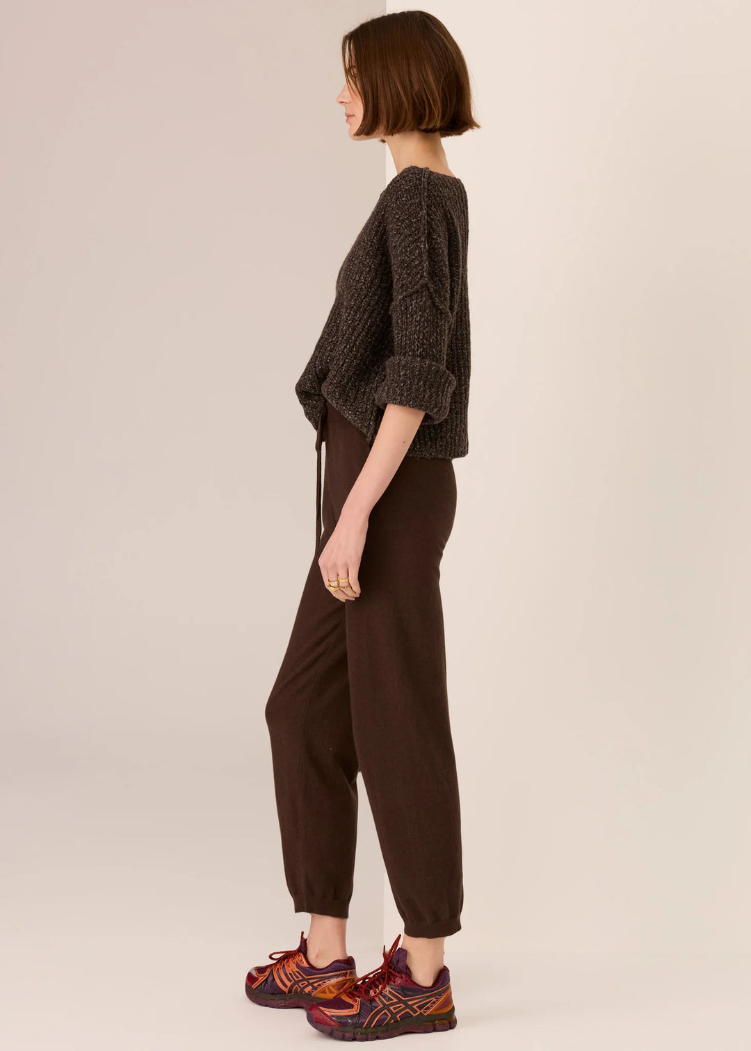 Person wearing a brown knitted sweater and pants on a beige background