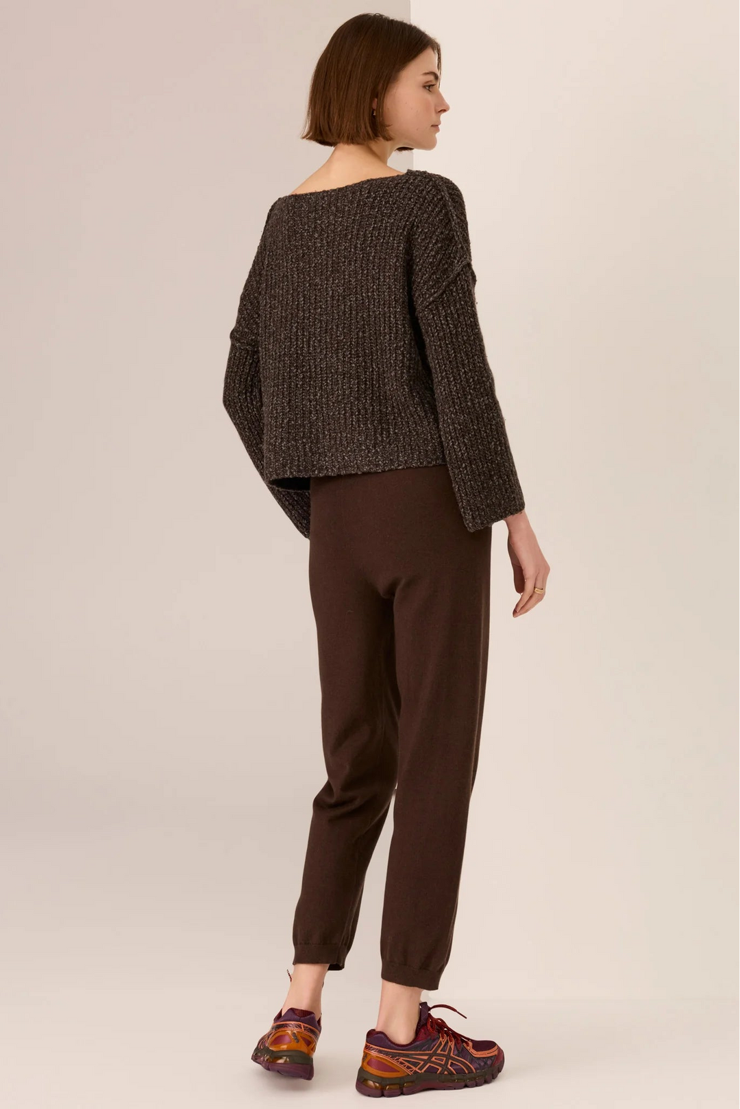 Woman wearing a dark brown textured sweater and brown pants on a beige background