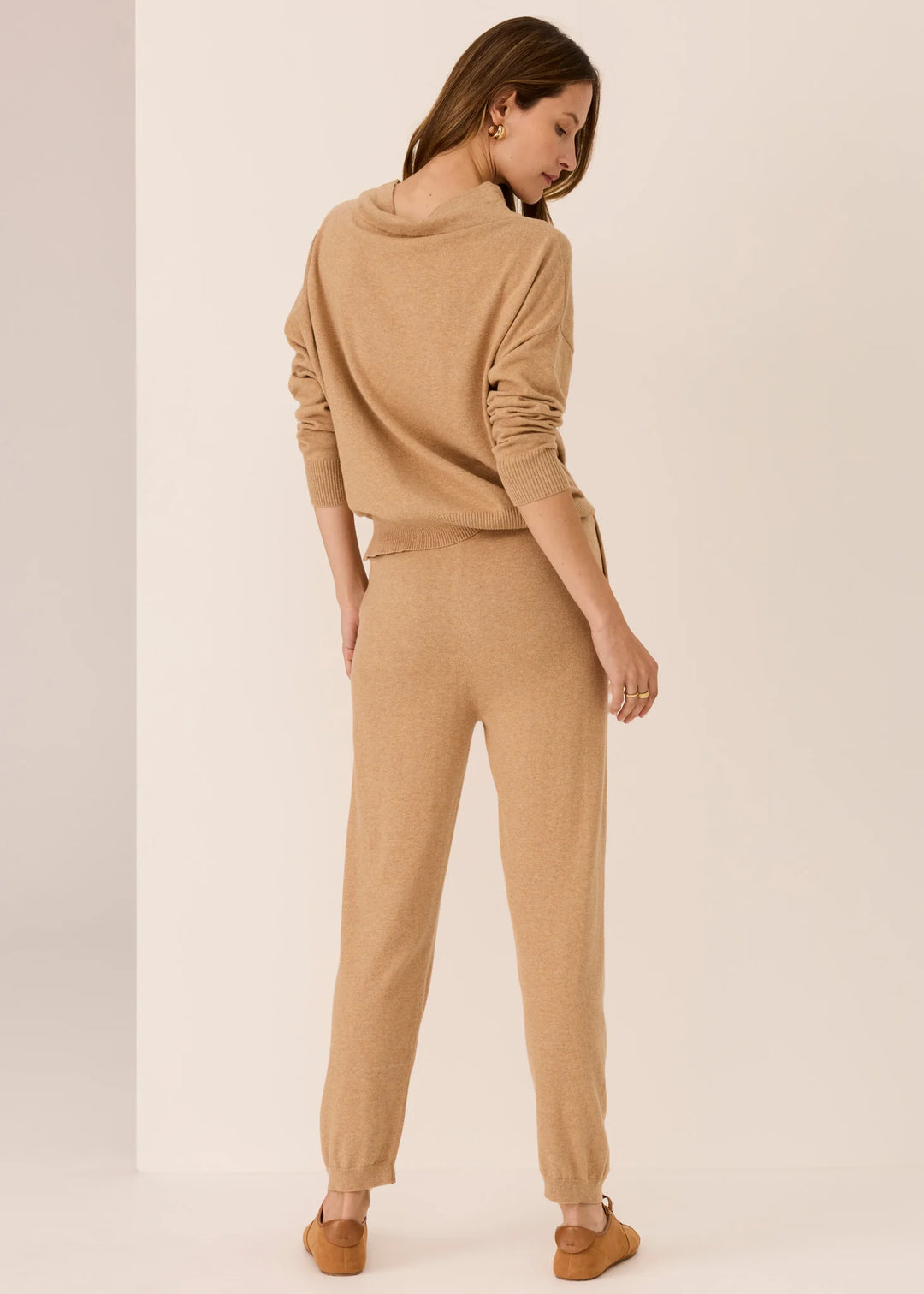 Woman wearing a beige sweater and pants on a plain background