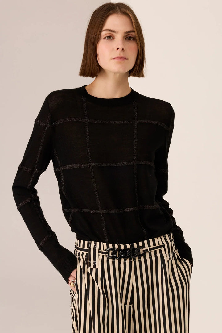 Woman wearing a black checkered sweater and striped pants on a beige background