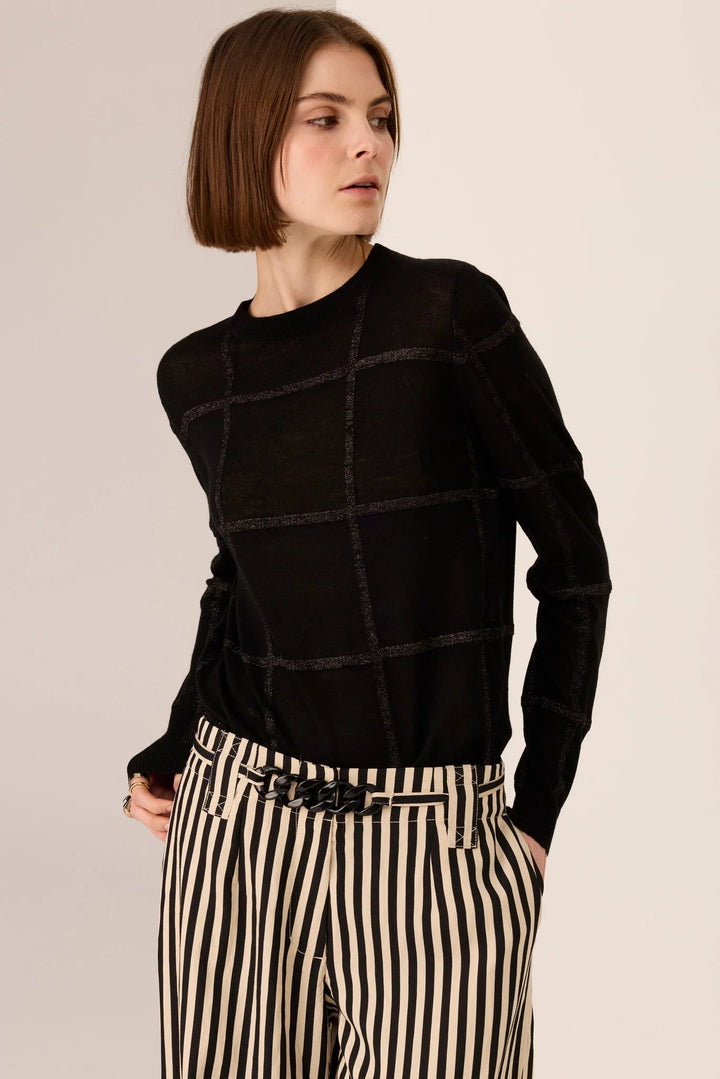Woman wearing a black sweater and striped pants on a beige background