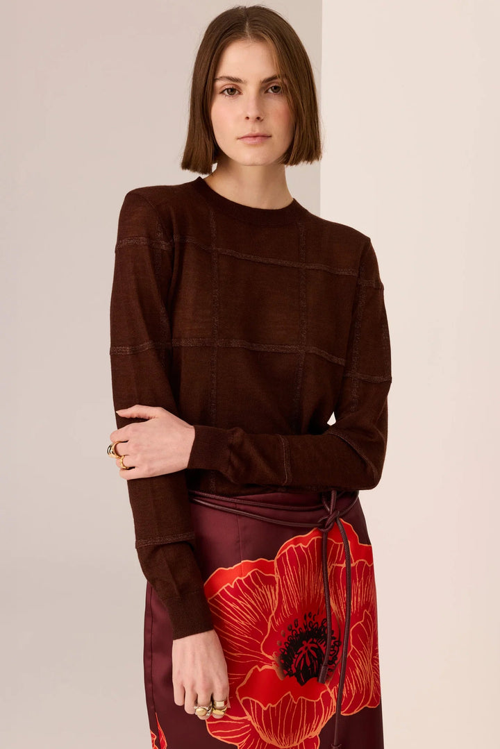 Woman wearing a brown long-sleeve top and a red floral skirt on a beige background