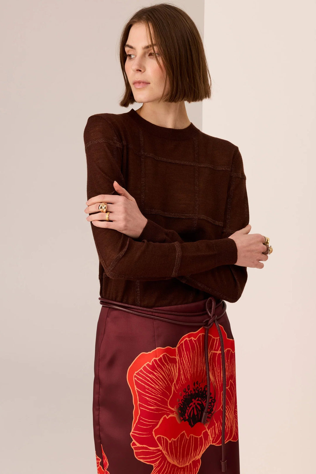 Woman wearing a brown top and red floral skirt against a beige background