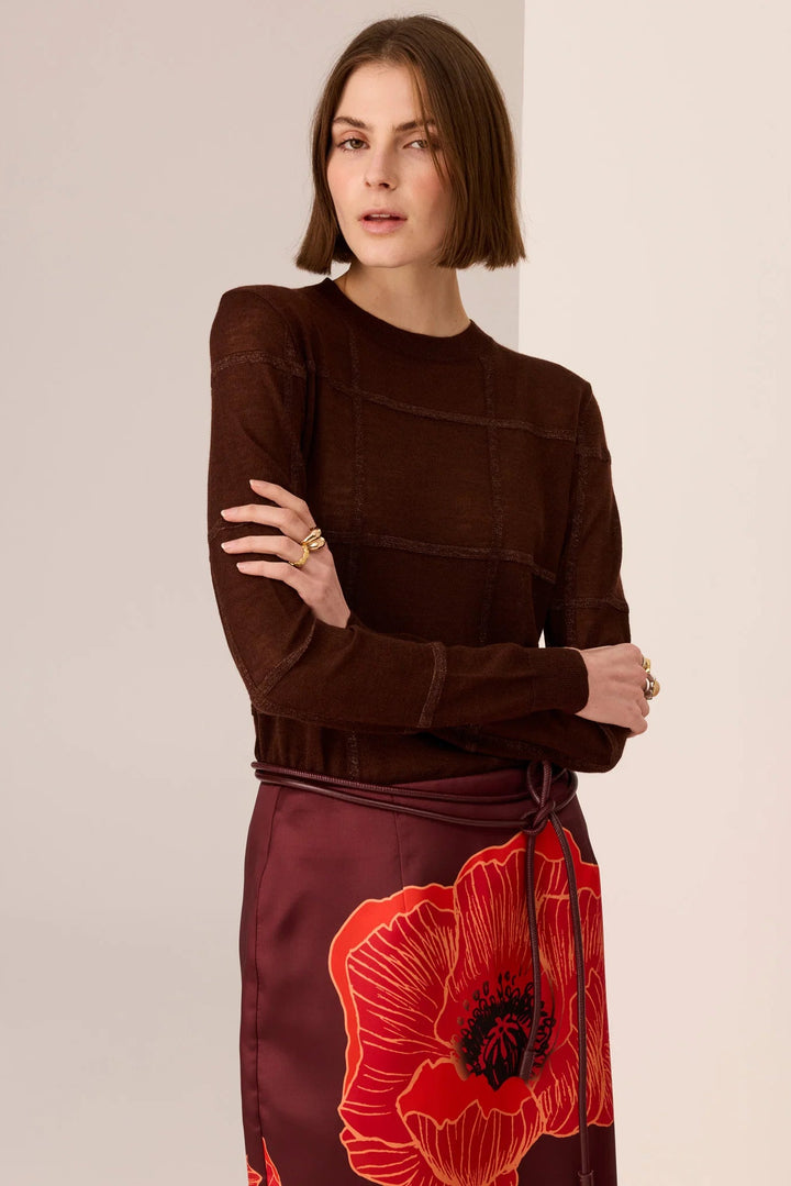 Woman wearing a brown top and red floral skirt against a plain background