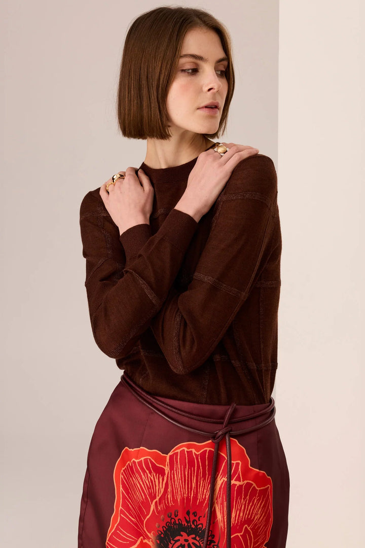 Woman wearing a brown top with a red floral skirt against a beige background