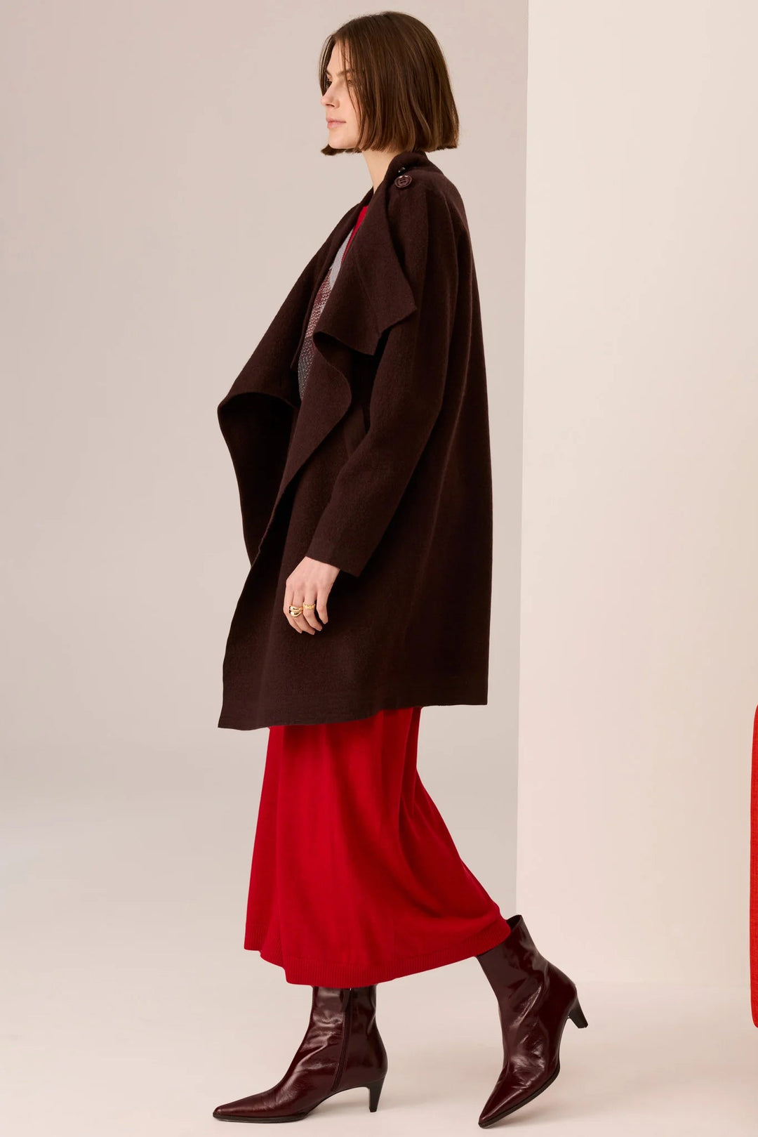 Woman wearing a brown coat and red skirt with a plain background