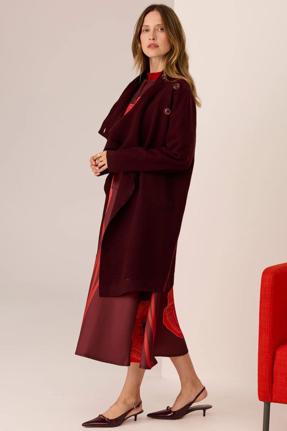 Woman wearing a burgundy coat with red accents on a plain background