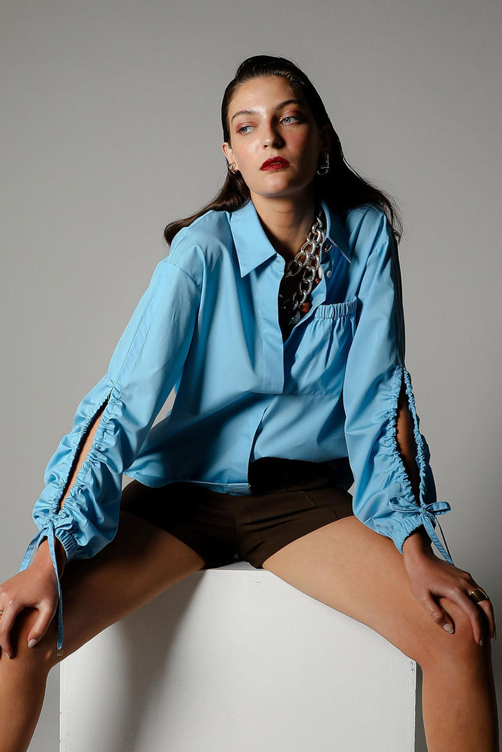 Woman wearing a blue shirt sitting on a white stool against a gray background