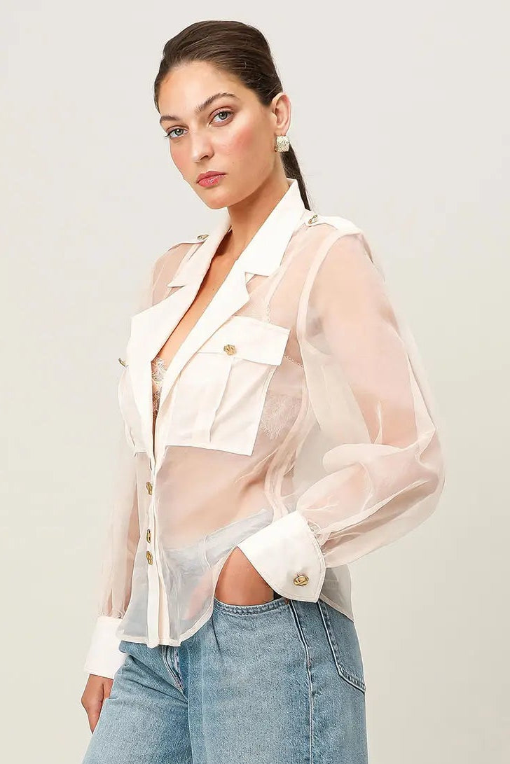 Woman wearing a sheer white blouse over a denim outfit on a plain background