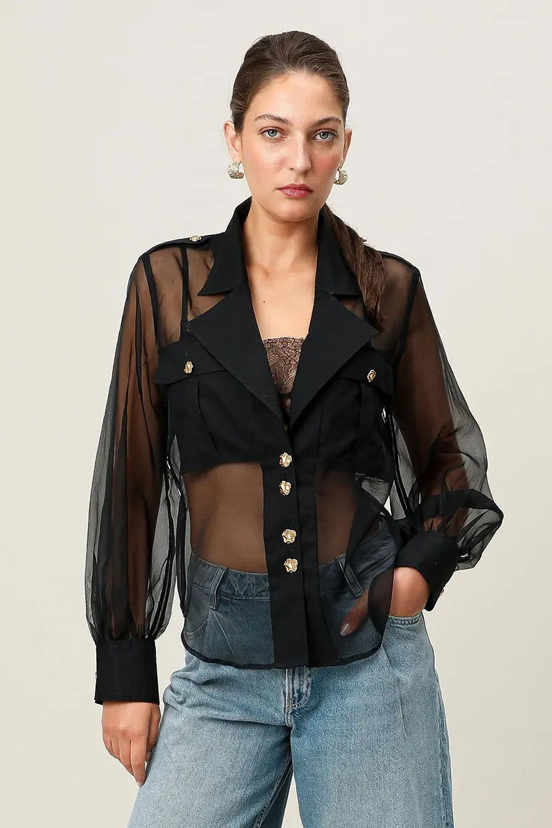 Woman wearing a black sheer jacket over a black top with blue denim shorts on a white background