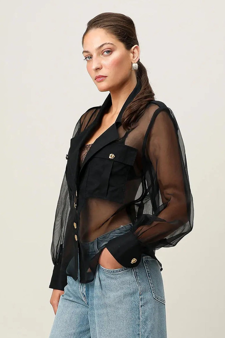 Woman wearing a black sheer jacket over a black top with denim shorts on a white background