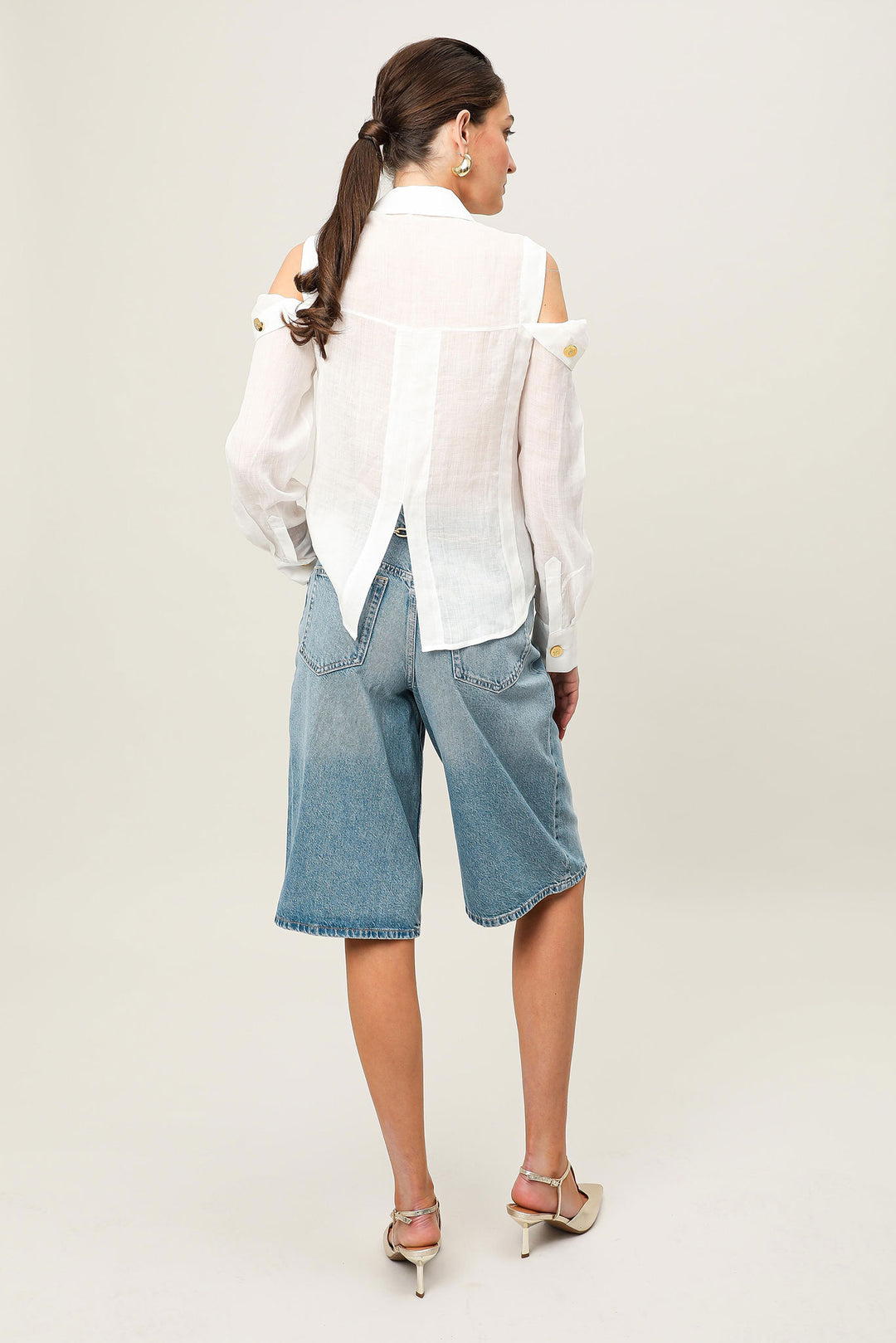 Woman wearing a white blouse and blue denim shorts on a plain background