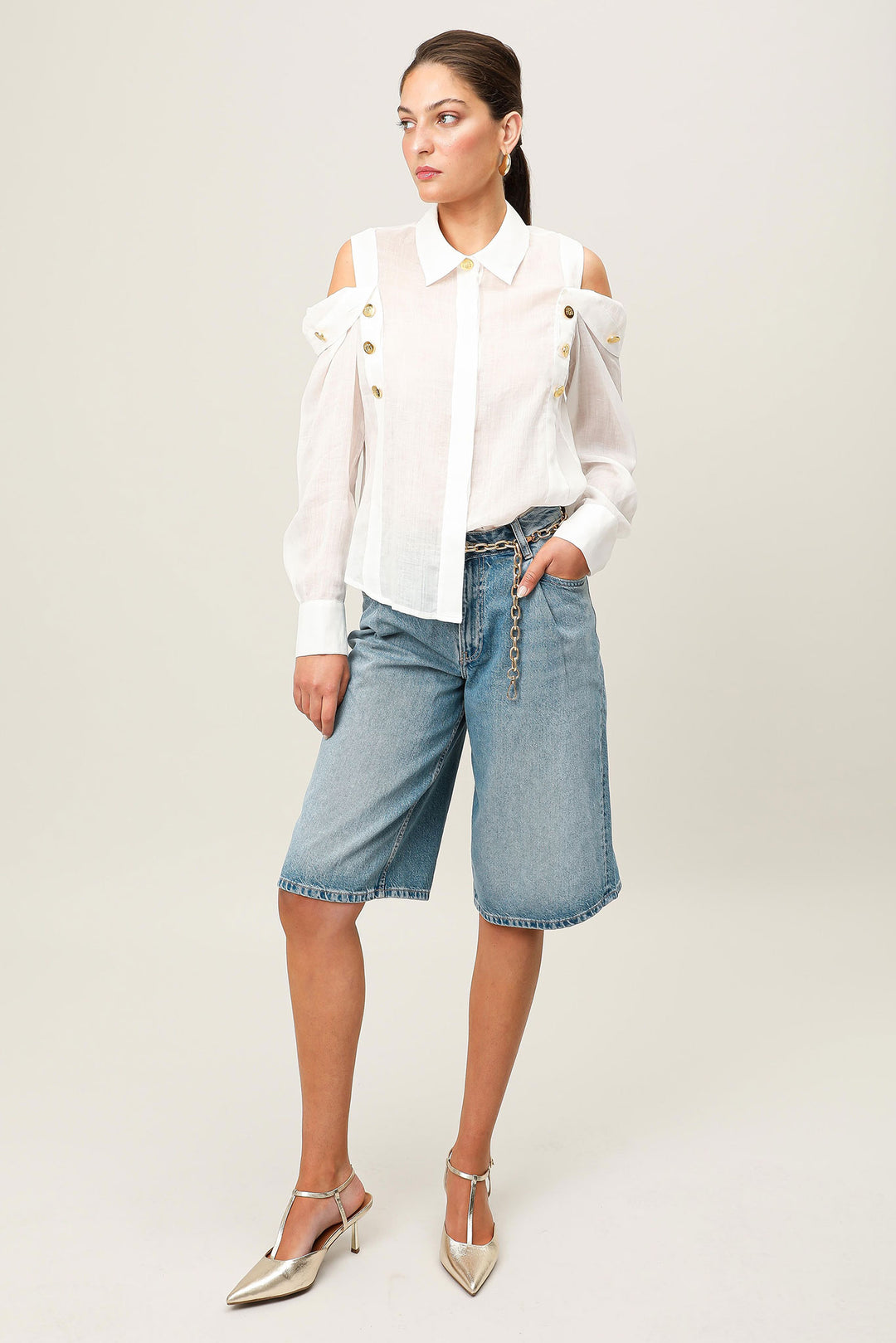 Woman wearing a white blouse and blue denim shorts on a plain background