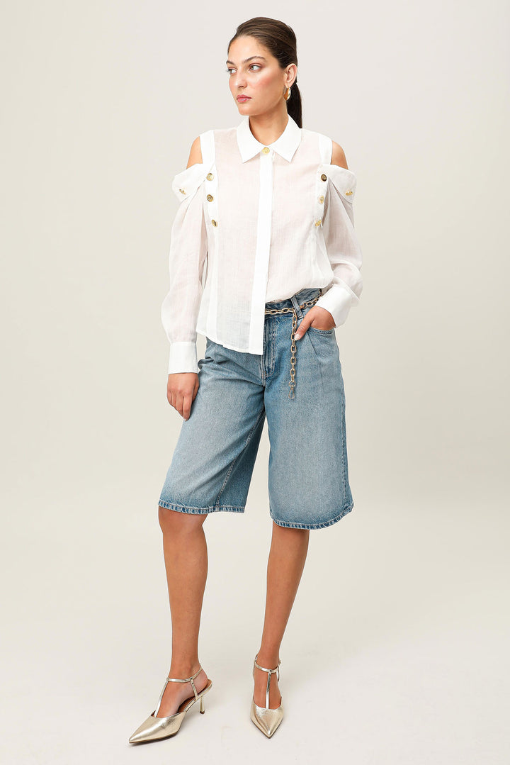 Woman wearing a white blouse and blue denim shorts on a plain background