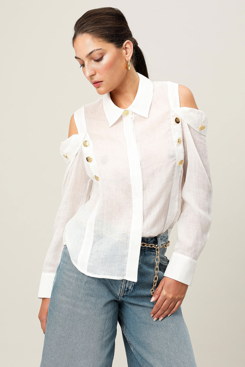 Woman wearing a white blouse with gold buttons and blue jeans on a plain background