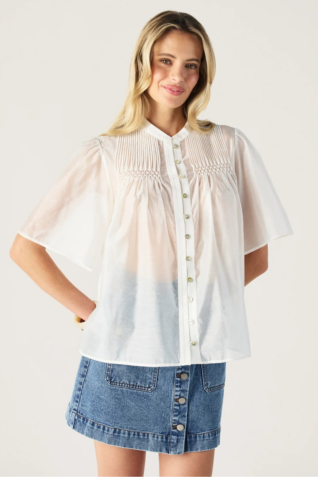 Woman wearing a white blouse with a gradient effect and a denim skirt on a plain background