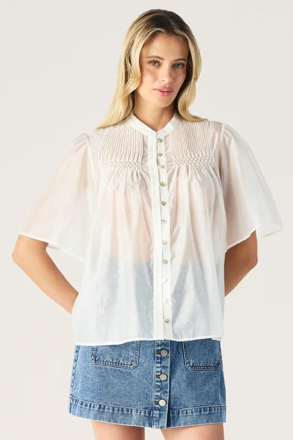 Woman wearing a white shirt with a gradient effect and denim shorts on a plain background