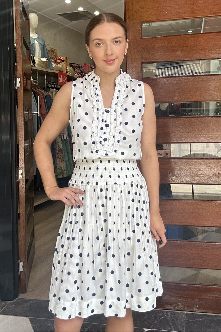 Woman in a white dress with navy polka dots standing in front of a store entrance.