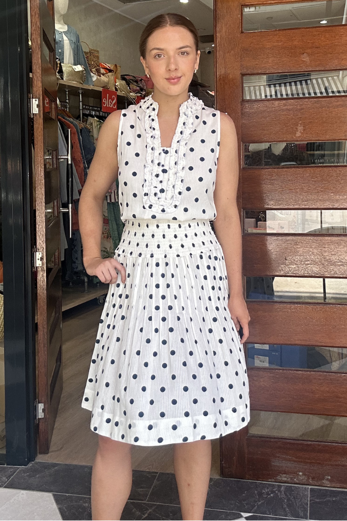 Woman in a white polka dot dress standing in front of a store entrance.