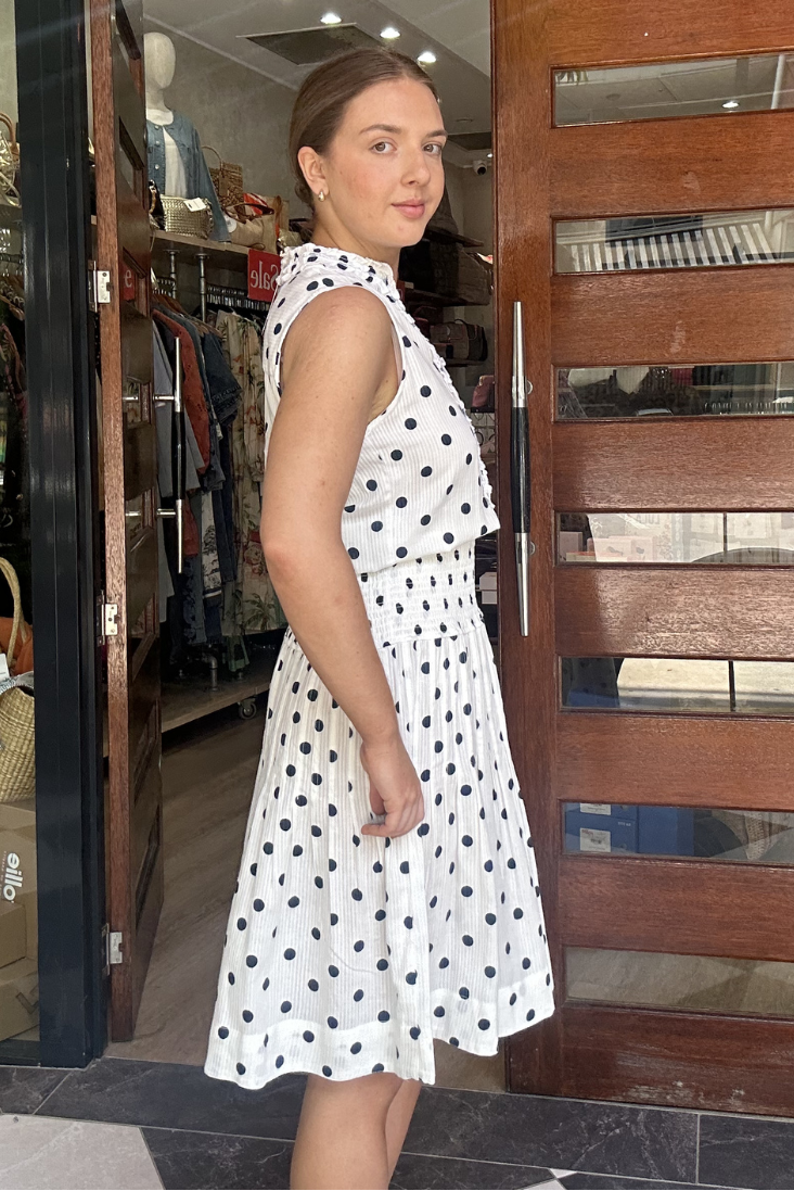 Woman in a polka dot dress standing in front of a store entrance.