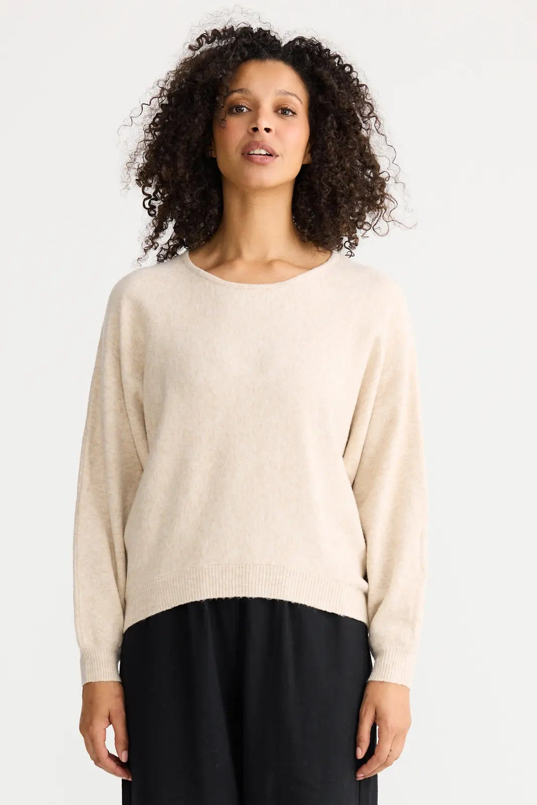 Woman wearing a beige sweater and black pants on a white background