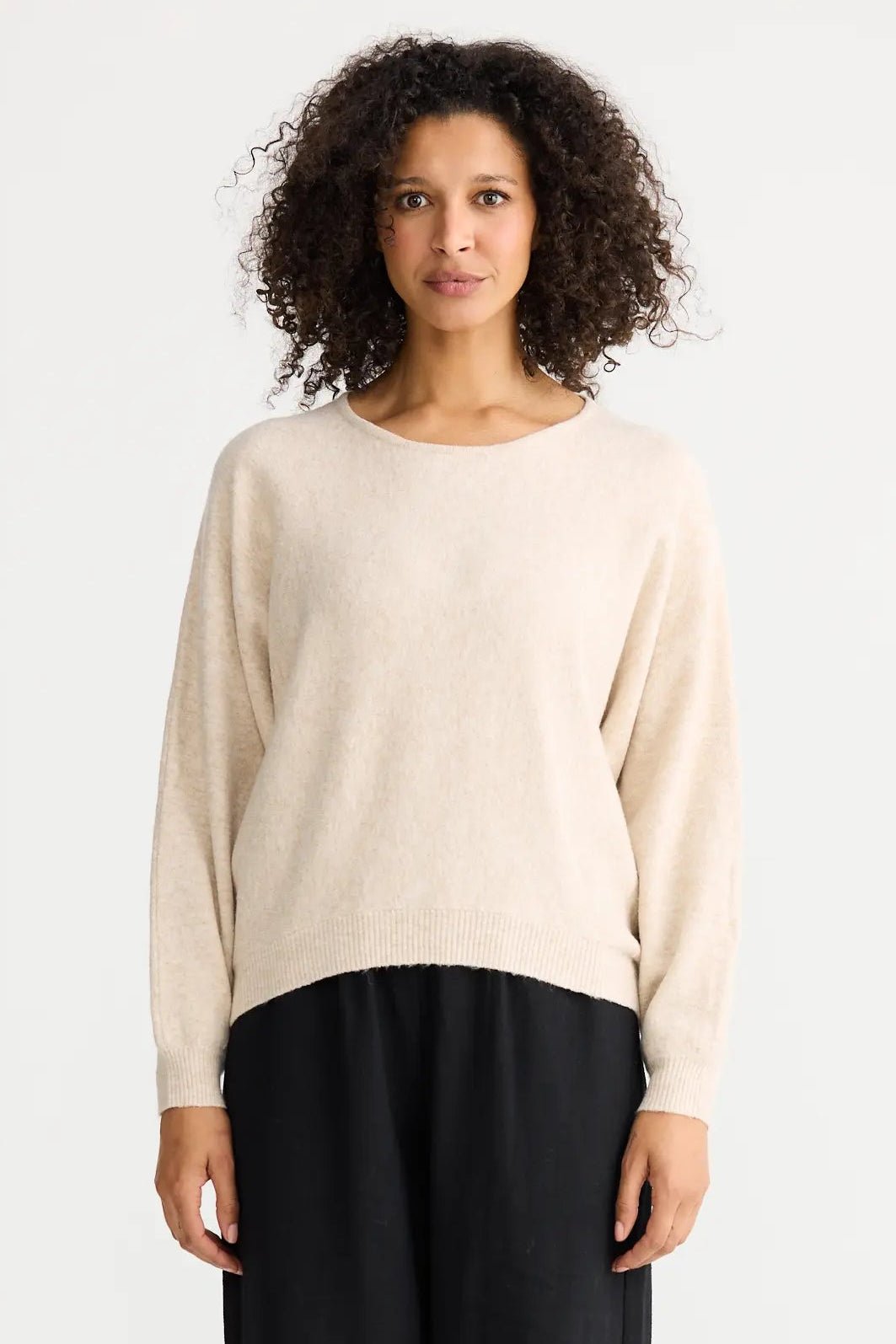 Woman wearing a beige sweater and black pants on a white background