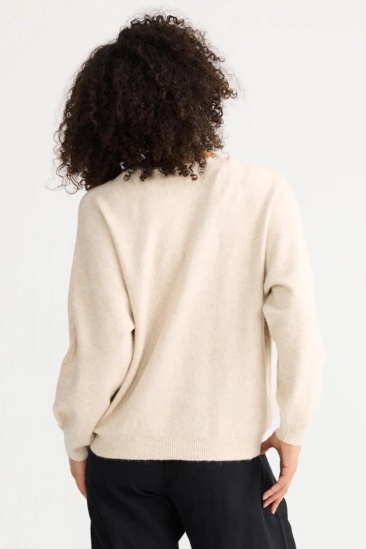 Person wearing a beige sweater and black pants on a white background