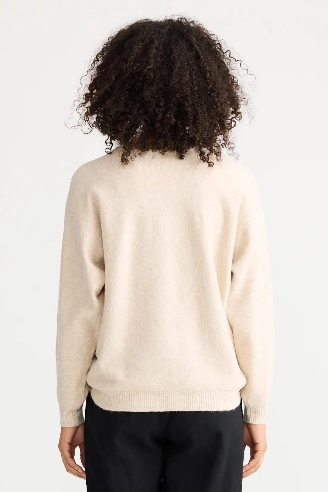 Person wearing a cream sweater and black pants on a white background