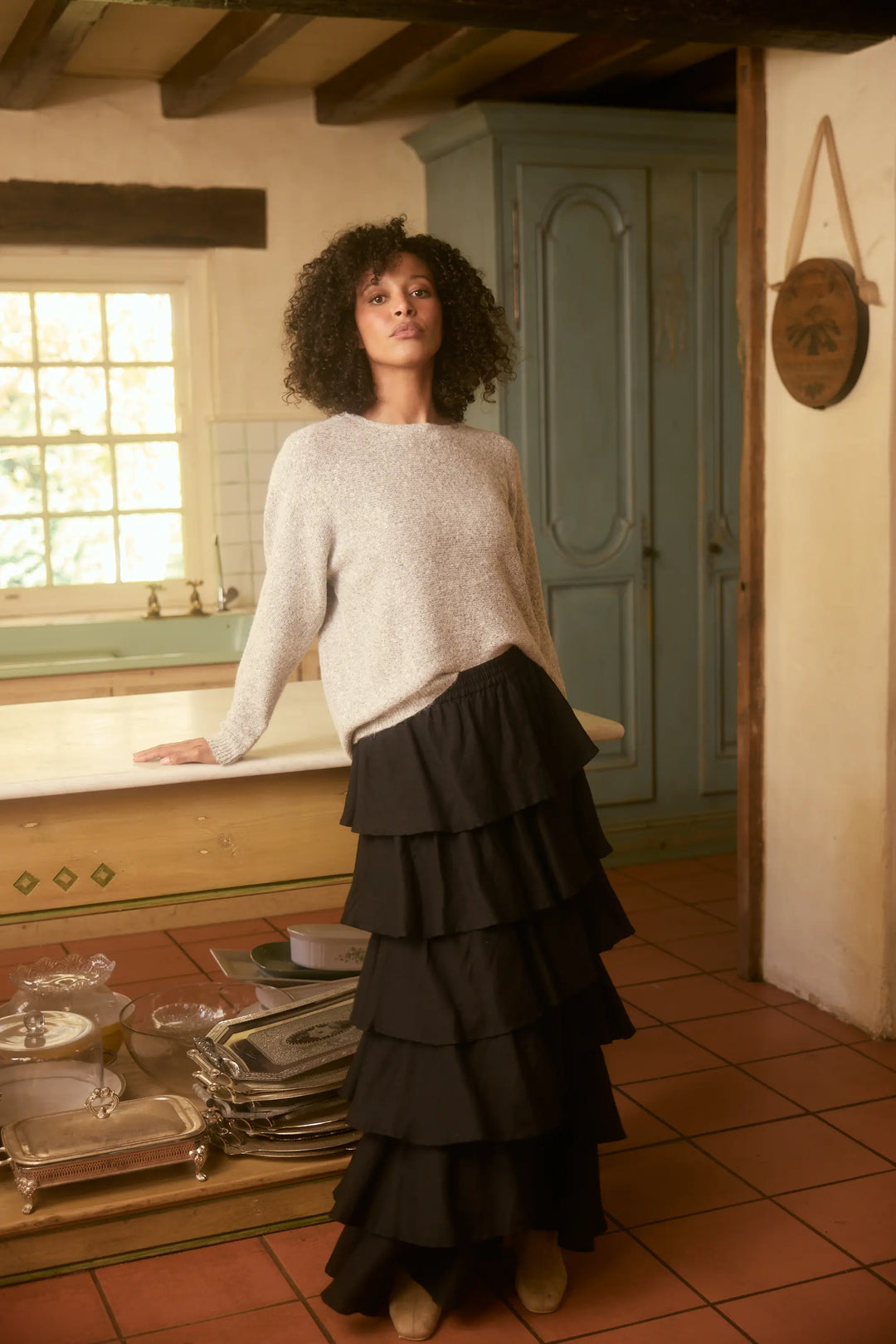 Woman in a kitchen wearing a light sweater and black tiered skirt.