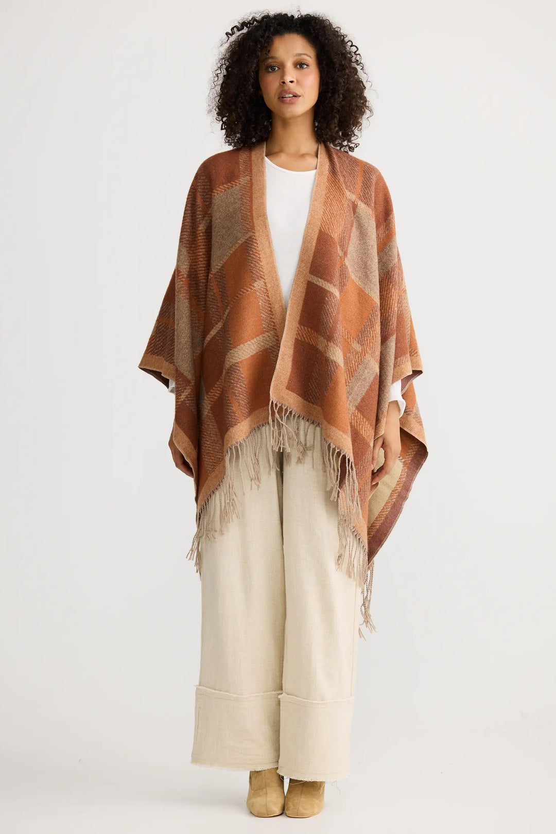 Woman wearing a patterned shawl over a white top and beige pants on a white background