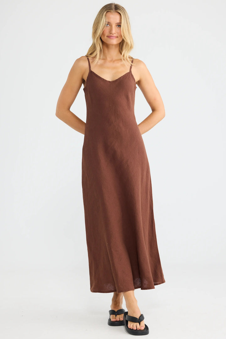 A woman modeling a brown spaghetti-strap maxi slip dress against a plain white studio background.