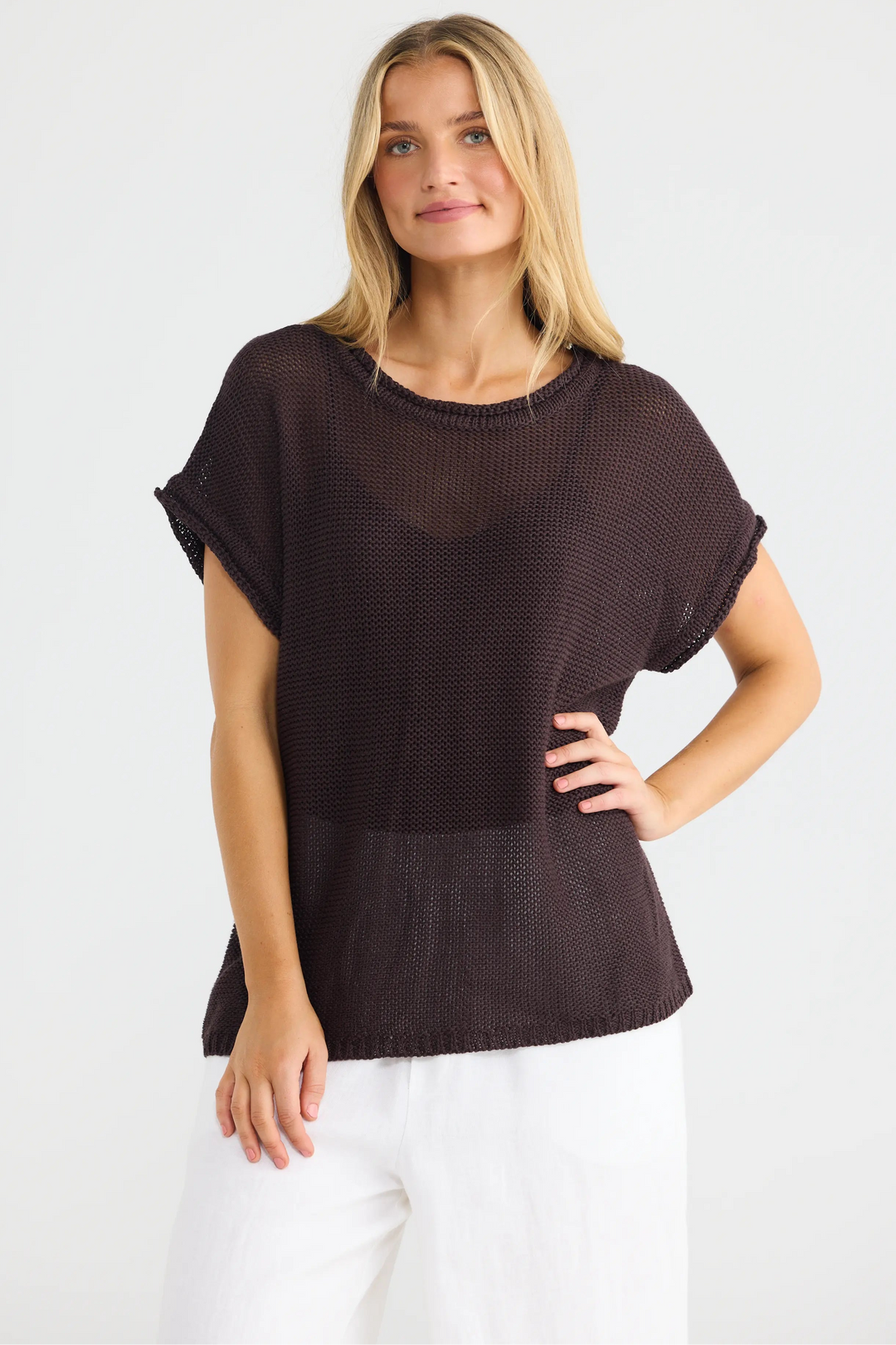 A woman modeling a dark brown short-sleeve knit top with a textured pattern, paired with white pants, against a plain white studio background.