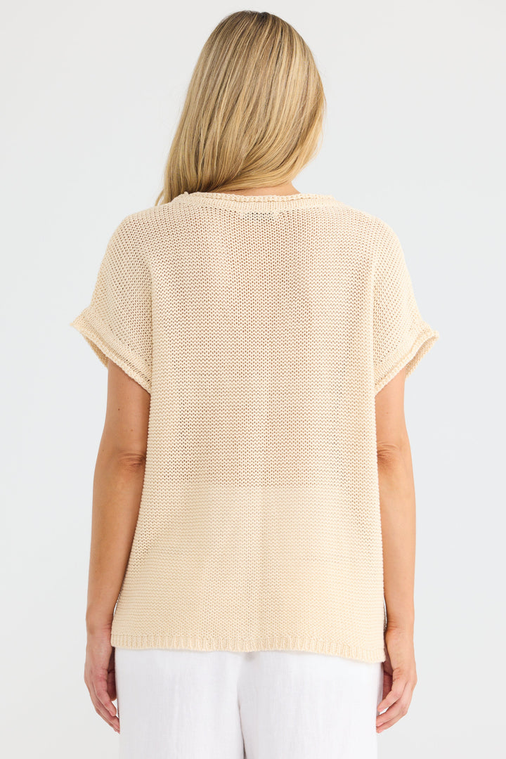 A woman viewed from behind wearing a short-sleeve cream-colored knit top and white pants against a plain white background.