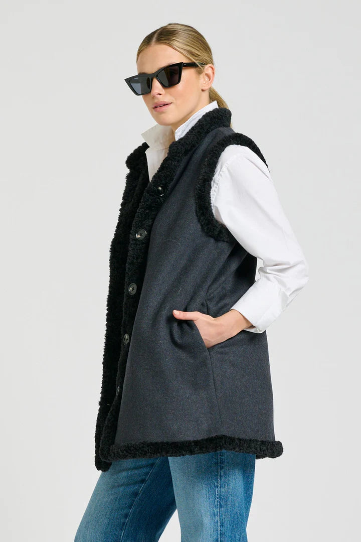 Woman wearing a dark gray vest with black trim on a light gray background
