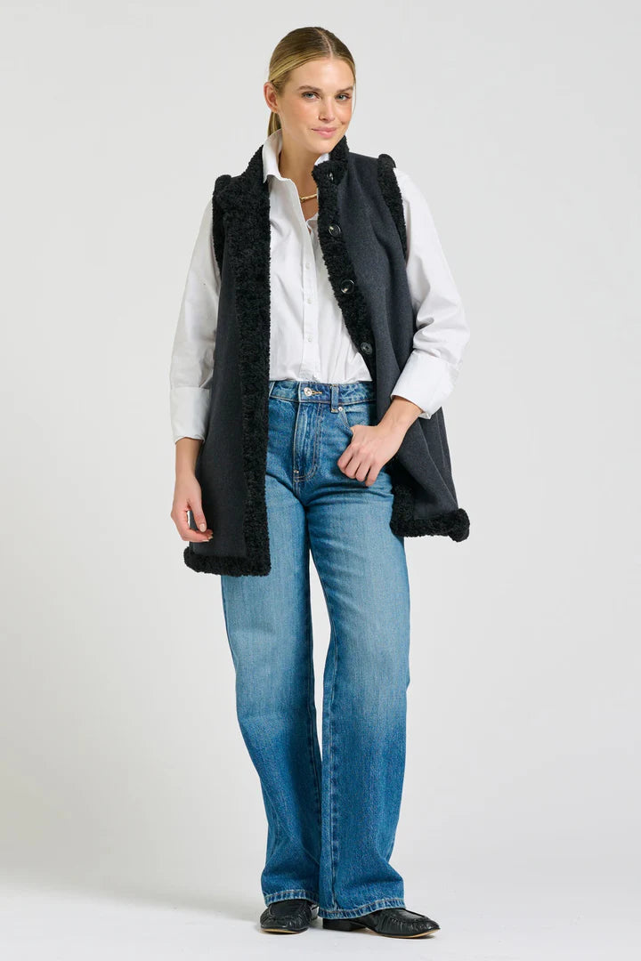 Woman wearing a black vest over a white shirt with blue jeans on a white background