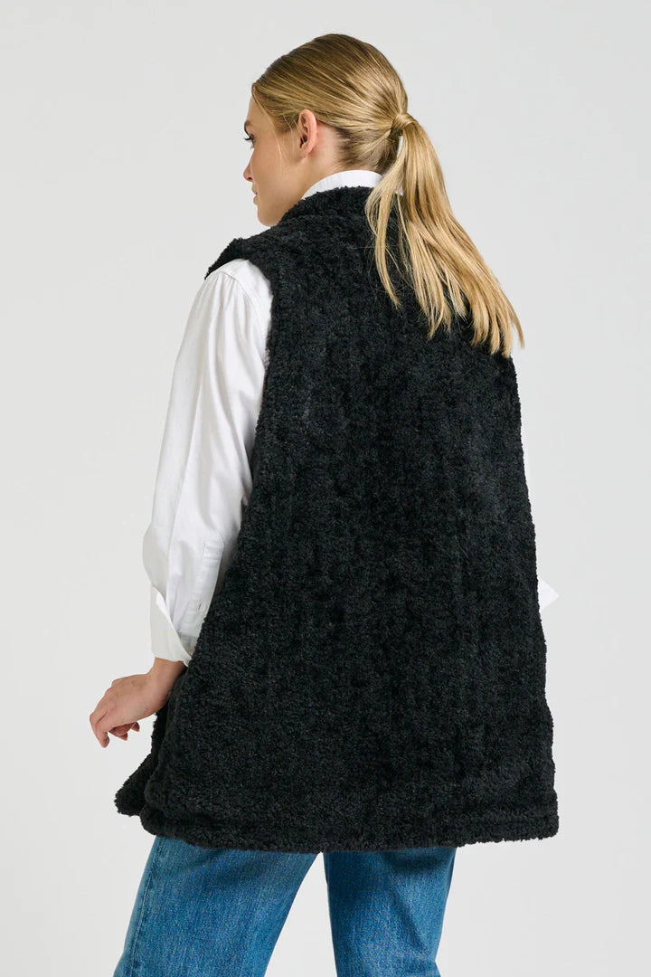 Person wearing a black knitted vest over a white shirt on a light gray background